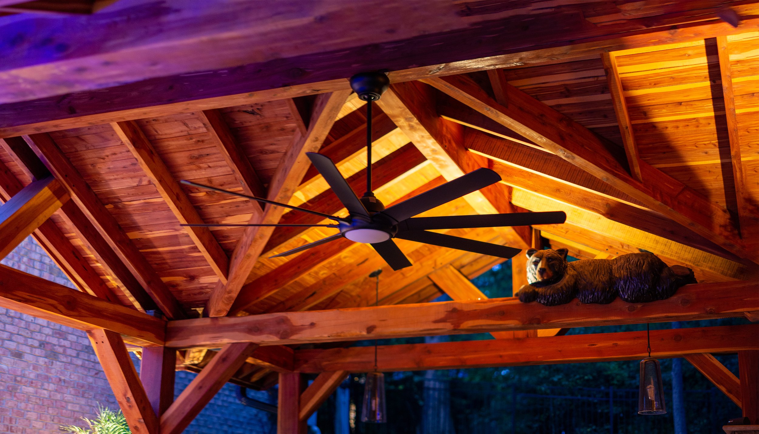 Outdoor kitchen and living area with lights illuminating the wooden ceiling of the outdoor structure.