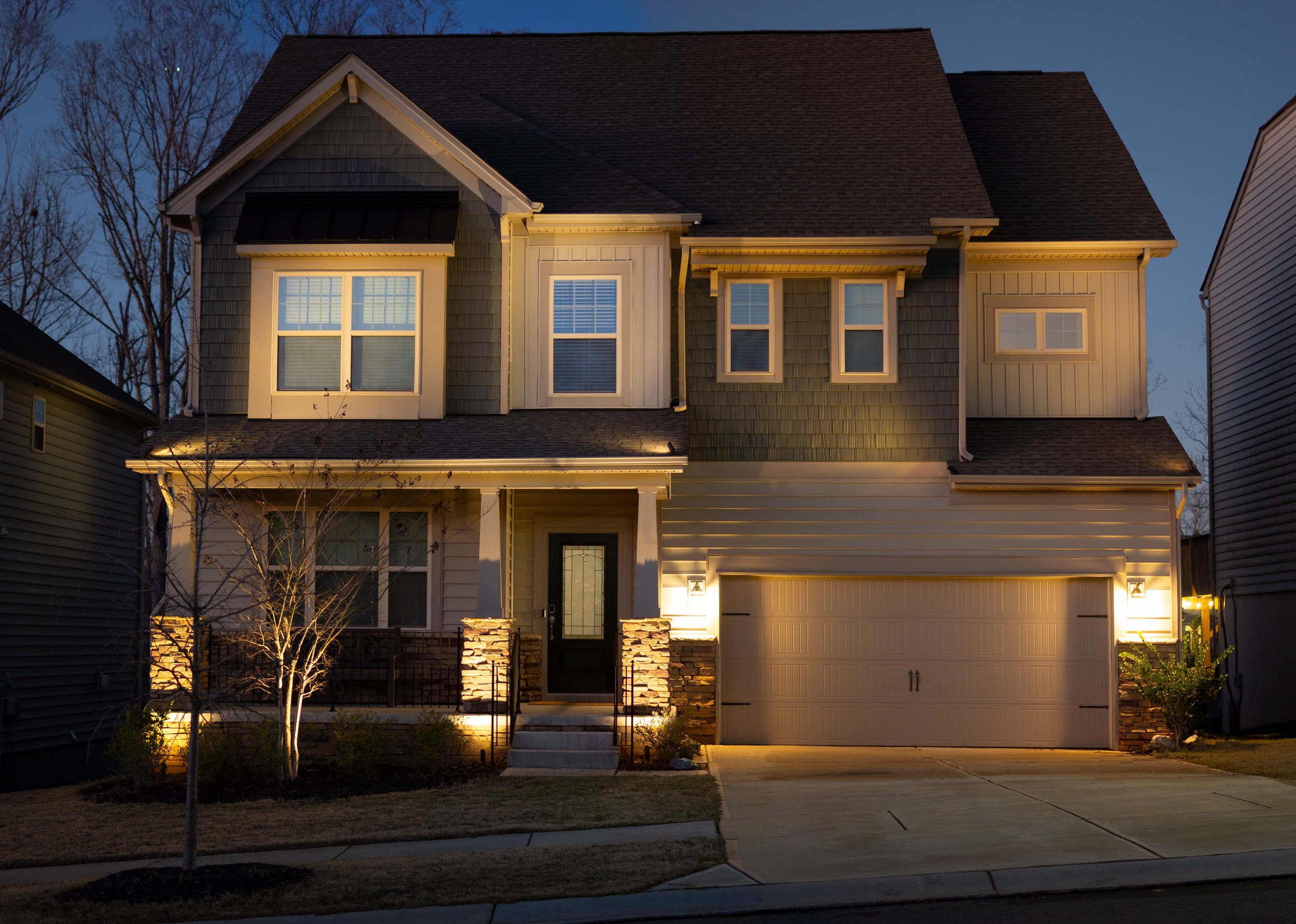 Green and tan craftsman style home illuminated with a combination of architectural up lights and landscape lighting. Small crepe myrtle with accent lights is positioned in front of the home.