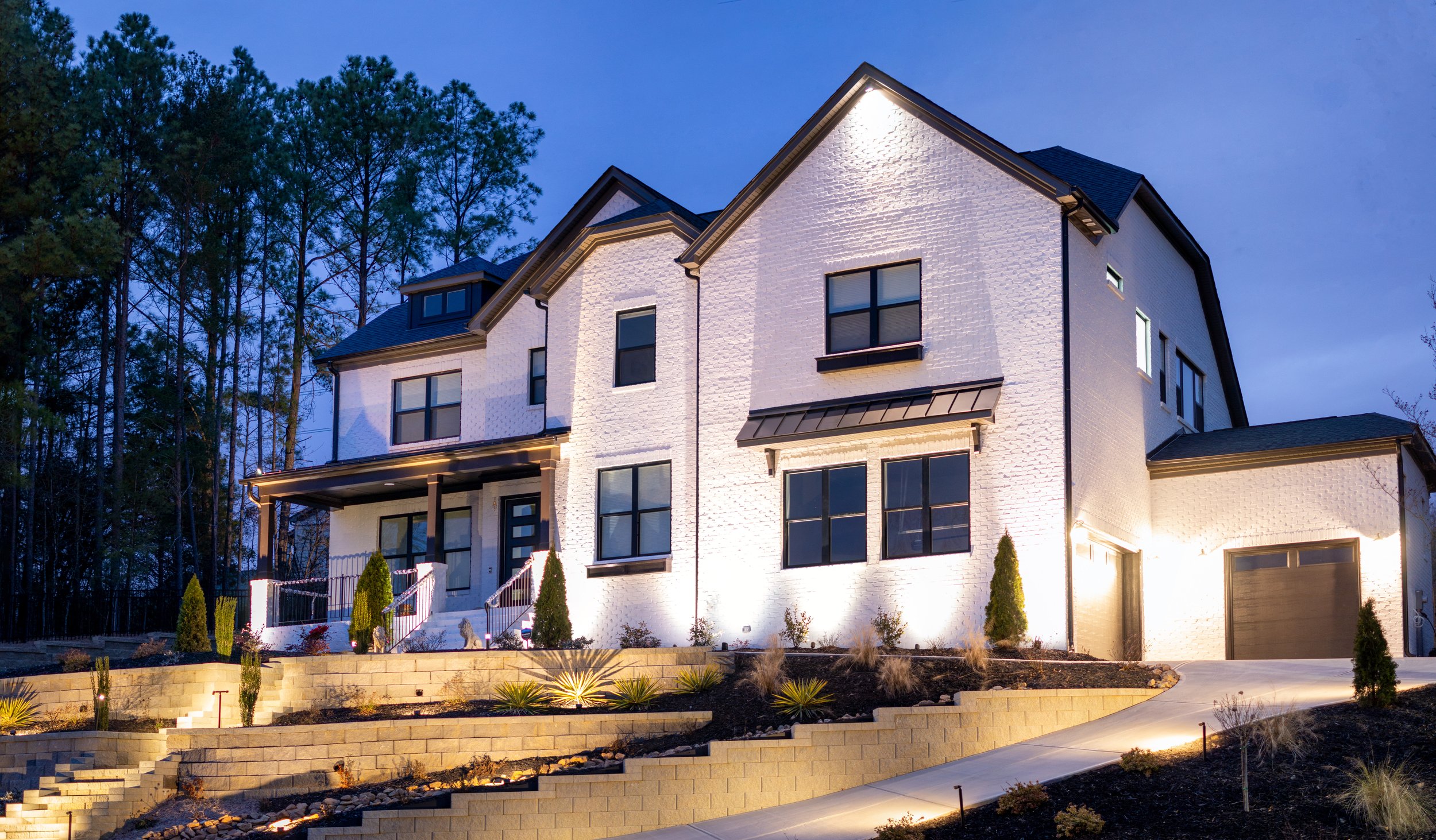 Modern light colored brick home illuminated with architectural landscape lighting. 