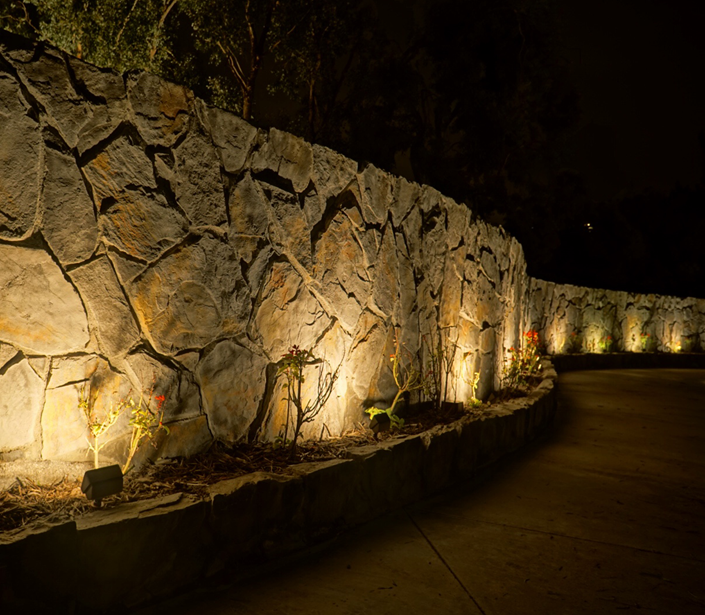 A curved natural stone landscaping wall is illuminated with a series of wall wash landscaping lights.