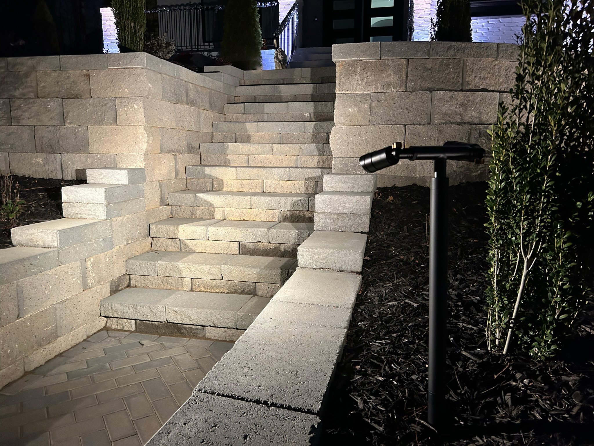 A multidirectional path light illuminates a set of stone stairs leading to the front entrance of the home.