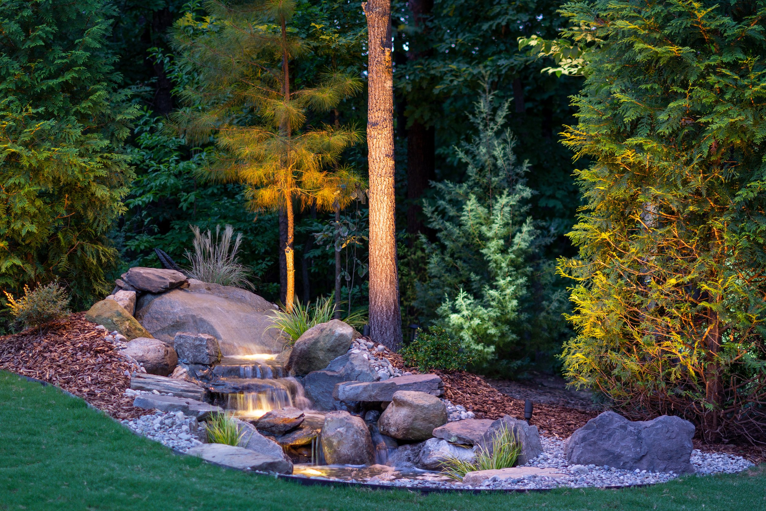 Small pond and waterfall feature illuminated with underwater lights and general landscape lighting. 